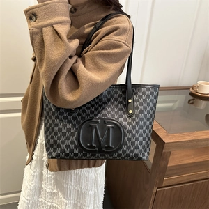 Close-up of black leather tote bag featuring repeating gray M pattern and large embossed logo