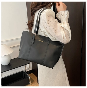 Black leather tote bag with gold lettering shown on shoulder for daily commute style