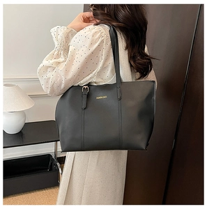 Detail of black leather tote bag featuring gold lettering and adjustable shoulder strap
