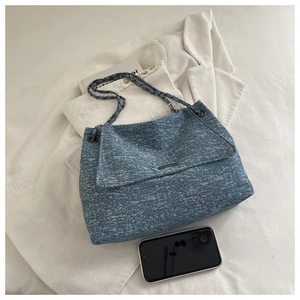 Détail du sac cabas en tweed bleu avec bandoulière chaîne et plaque logo en métal