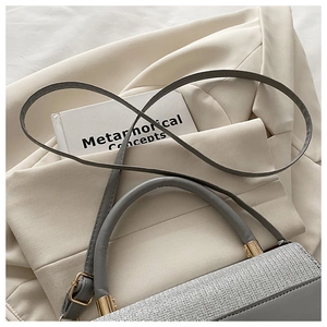 Close-up of grey leather and tweed handbag with elegant gold buckle and adjustable strap