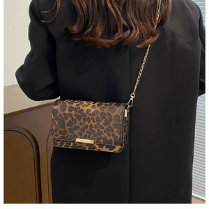 Detail of leopard print crossbody bag with gold buckle and chain strap on a black blazer