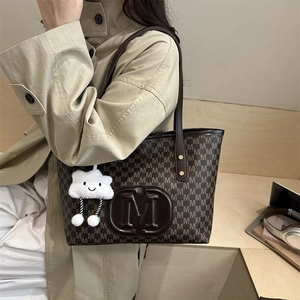 Detail of printed tote bag with large M logo and cute cloud charm on shoulder strap