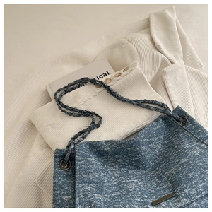 Détail du sac en denim bleu à chaîne avec plaque métallique sur un blazer blanc