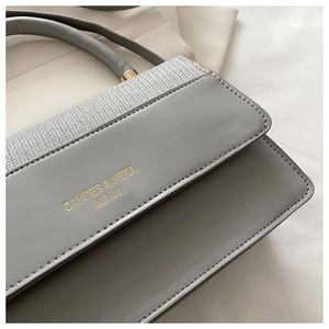 Detail of grey leather tote showing silver-grey woven texture and gold brand logo