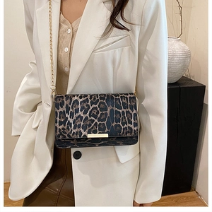 Detail of leopard print crossbody bag with gold chain strap worn over a white blazer