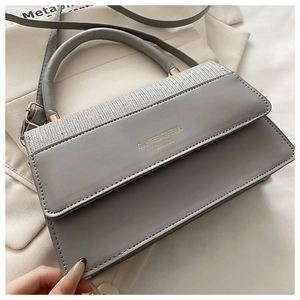 Detail of silver woven texture and gold brand logo on the grey leather square bag