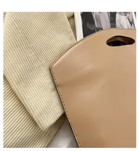 Detail view of beige leather handbag with cutout handle and precise stitching