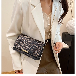 Detail of leopard print crossbody bag with gold chain strap and metal trim on white blazer