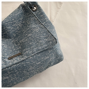Détail du cabas en jean délavé bleu clair avec bandoulière chaîne et garniture métal