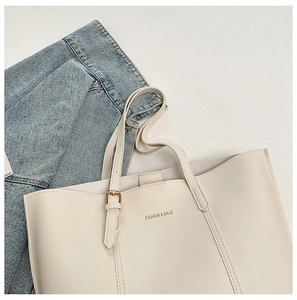 Detail of a large cream tote bag with golden branding and extended shoulder straps