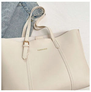 Detailed close-up of a beige tote bag showing texture, gold logo, and fine stitching