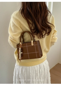 Close-up of brown quilted tote bag with white stitching and decorative beaded tassel