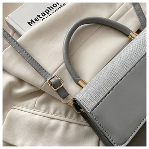 Detail view of grey leather handbag with woven texture flap and golden hardware