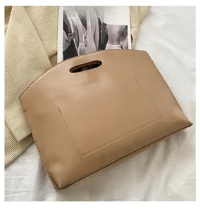 Close-up of light brown matte leather handbag with trapezoidal silhouette on white linen