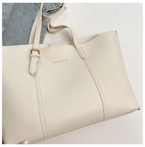 Detailed close-up of cream tote bag featuring golden fashion text and premium metal buckles