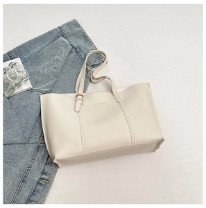 Detailed shot of a beige PU leather tote bag with gold lettering on denim jeans background