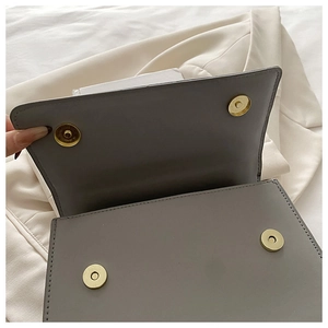 Detail view of grey flap bag showing dual gold magnetic closures and matte leather texture