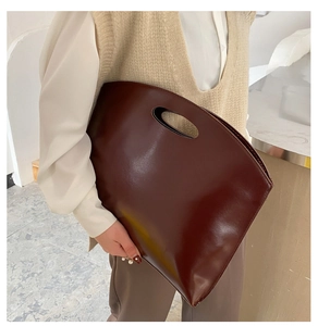 Detail of a dark brown tote bag with a unique cutout handle and minimalist design