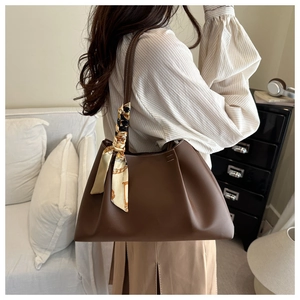 Détail d'un grand sac cabas marron en cuir avec plis latéraux et foulard en soie