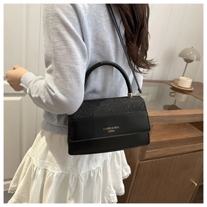 Detail of black leather handbag with glitter flap and golden logo in a lifestyle setting