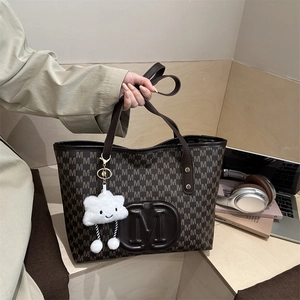 Brown monogram tote bag with leather handles and white plush charm on a wooden desk