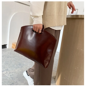 Detail of a minimalist dark brown leather handbag with a unique cut-out semi-circular handle