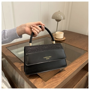 Detail of a black flap handbag featuring sequined texture and golden brand logo accents