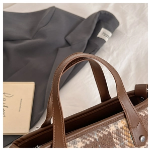 Détail macro du sac cabas à carreaux marron avec anses en cuir et rivets argentés