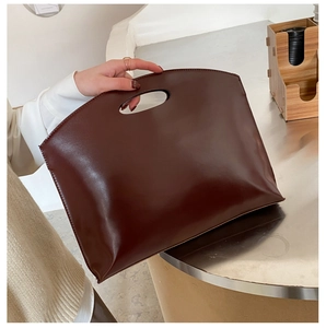 Detail of minimalist dark brown leather handbag featuring a smooth finish and cutout handle