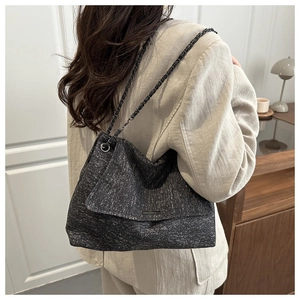 Détail d'un grand sac cabas gris foncé avec chaîne en métal porté à l'épaule du modèle