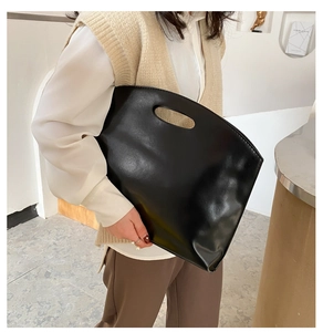 Minimalist black faux leather clutch bag with cutout handle shown in a lifestyle setting