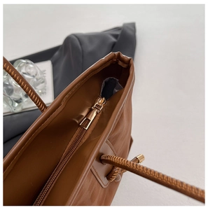 Macro shot of gold-tone zipper closure and metallic strap rings on brown leather tote bag