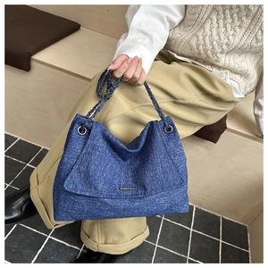 Détail du sac cabas en denim bleu avec barre en métal et bandoulière en chaîne classique