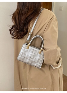 Piccola borsa quadrata argento con trama a griglia e manico in metallo su trench beige