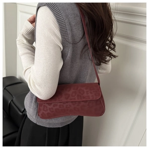 Detail of dark wine red baguette bag with leopard embossing and slim shoulder strap