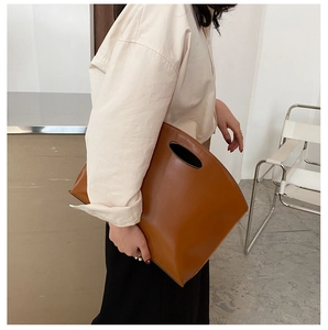 Detail of minimalist brown leather clutch bag with oval handle and smooth oil finish