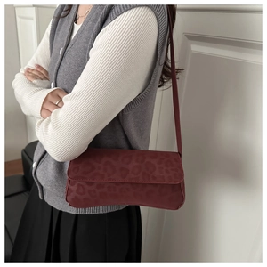 Detail of burgundy baguette bag with leopard embossing and slim leather shoulder strap