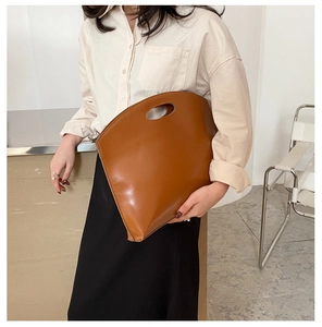 Detailed view of a brown minimalist oversized clutch bag with an oval cutout handle