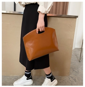 Detailed view of brown leather handbag with unique cutout semicircular handle