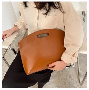 Detail of a brown leather clutch with oval cutout handle and unique semi-circular top design