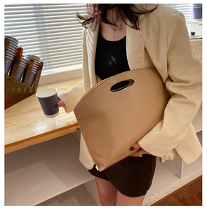 Minimalist khaki leather tote bag featuring a unique oval cutout handle in a scenic setting