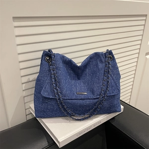 Grand sac cabas en jean bleu avec bandoulière en chaîne et rabat sur décor blanc