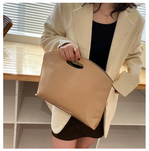 Minimalist beige leather tote bag with cut-out handle styled in a business office setting