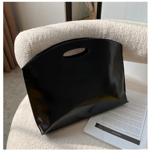 Close-up of a minimalist black leather tote bag with oval cut-out handle on a cozy chair