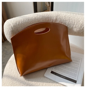 Detail of caramel leather tote bag with unique oval cutout handle on white chair