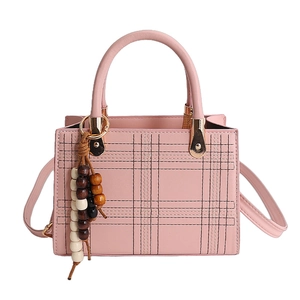 Pink quilted faux leather crossbody bag with wooden bead charm on white background