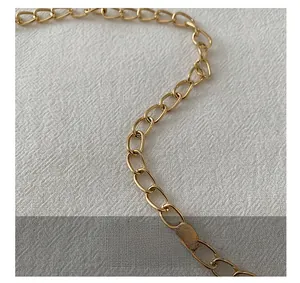 Détail de la bandoulière en chaîne dorée champagne sur un tissu blanc texturé