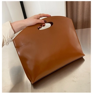 Detail view of caramel brown leather handbag with minimalist cutout handle and stitching