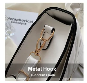 Detail of light gold hardware hook on a white PU leather shoulder bag with black edges